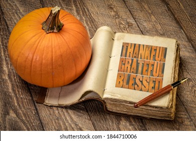 thankful, grateful and blessed inspirational words in vintage letterpress wood type in a retro, leather-bound journal with a pumpkin against rustic wood, Thanksgiving theme