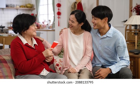 Thankful Young Couples Giving Chinese New Year Red Packet Lucky Money To Senior Mother During Their Visit On Spring Festival In A Modern Bright Living Room At Home