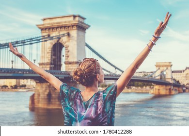 Thankful young redhead woman arms raised at Chain Bridge, Budapest, Hungary
