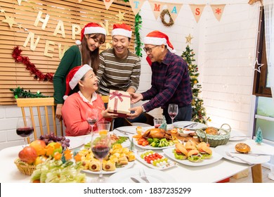 Thanksgiving Or Christmas Celebration Asian  Family Dinner Concept.Asian Happy Family Celebrating Christmas With Grandparents While Sitting Over Dining Chair And Wearing Santa Hat And With  Gift Box.