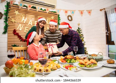 Thanksgiving Or Christmas Celebration Asian  Family Dinner Concept.Asian Happy Family Celebrating Christmas With Grandparents While Sitting Over Dining Chair And Wearing Santa Hat And With  Gift Box.