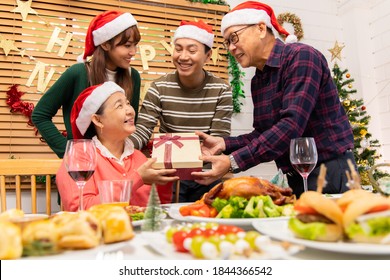 Thanksgiving Or Christmas Celebration Asian  Family Dinner Concept.Asian Happy Family Celebrating Christmas With Grandparents While Sitting Over Dining Chair And Wearing Santa Hat And With  Gift Box.