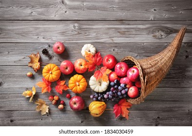 Thanksgiving cornucopia filled with pumpkins, apples, grapes and leaves on a rustic wooden background  - Shutterstock ID 1834030459