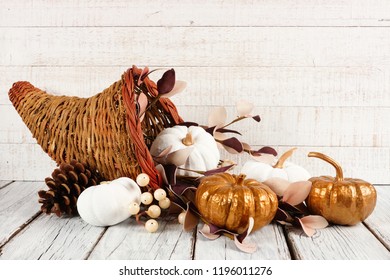 Thanksgiving Cornucopia Filled With White And Gold Pumpkins Against A White Wood Background