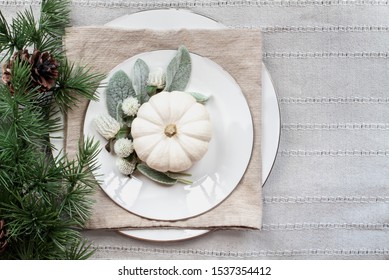 Thanksgiving Day Or Christmas Place Setting With White Plates, Mini White Pumpkins, Lamb's Ears Leaves, Fowers And Pine Branch Over Grey Table Runner.