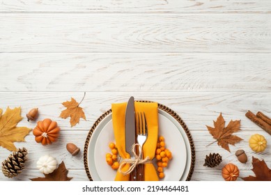 Thanksgiving day concept. Top view photo of plate cutlery fork knife napkin rowan maple leaves pine cones acorns pumpkins and cinnamon sticks on isolated white wooden table background with copyspace