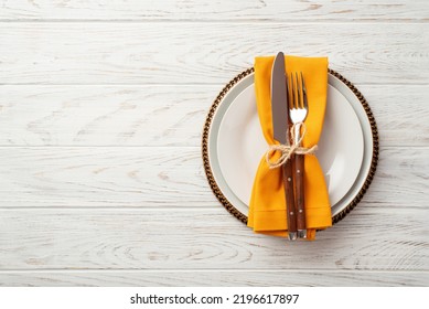 Thanksgiving Day Concept. Top View Photo Of Table Setting Plate Knife Fork And Orange Napkin On Isolated White Wooden Table Background