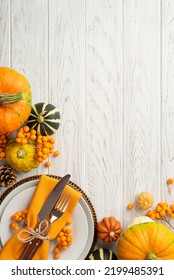 Thanksgiving Day Concept. Top View Vertical Photo Of Plate Knife Fork Napkin Raw Vegetables Pumpkins Pattypans Pine Cone And Rowan Berries On Isolated White Wooden Table Background