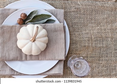 Thanksgiving Day or Halloween place setting with mini white pumpkins, Lamb's Ears leaves, and acorns over burlap table runner.