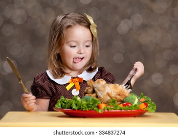 Thanksgiving Dinner.  Adorable Little Girl Sitting At A Small Table With A Small Turkey (chicken) On A Bed Of Greens And Other Vegetables.  Room For Your Text.