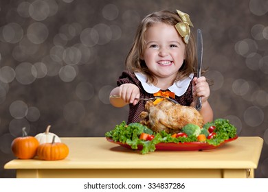 Thanksgiving Dinner.  Adorable Little Girl Sitting At A Small Table With A Small Turkey (chicken) On A Bed Of Greens And Other Vegetables.  Room For Your Text.