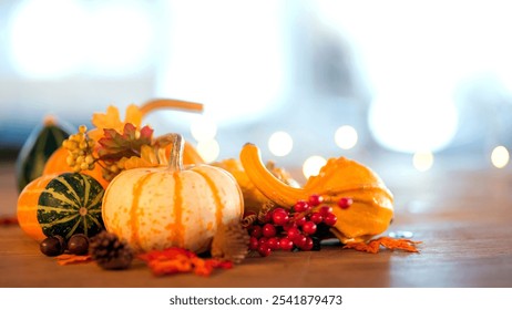 Thanksgiving display with pumpkins, gourds, fall foliage, red berries, pine cones, and acorns on a wooden surface. Soft-focus blue and white background creates warm autumn ambiance - Powered by Shutterstock