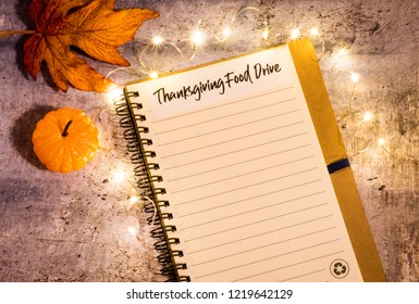 Thanksgiving Food Drive List Concept On Notebook Surrounded With Bright Leaves And Decorative Lights, Flat Lay