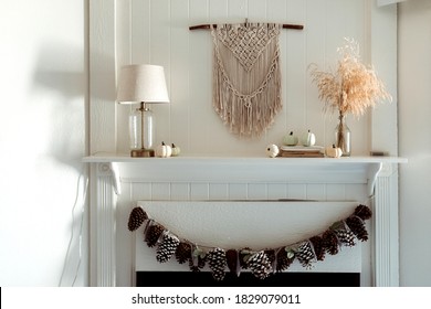 Thanksgiving Home  Decor - White Wooden Fireplace With Wall Macrame, Cream And Beige Pumpkins, Pine Cones Garland And Rustic Dry Wheet Bouquet. House Fall Decoration.