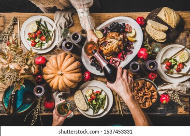 Thanksgiving party table setting. Flat-lay of people pouring champagne and celebrating at table with roasted chicken, vegetables, fig pie, fruit, candles over wooden table background, top view