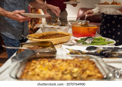 Thanksgiving Potluck With Family Gathered Aroudn The Food, Serving Themselves Dinner