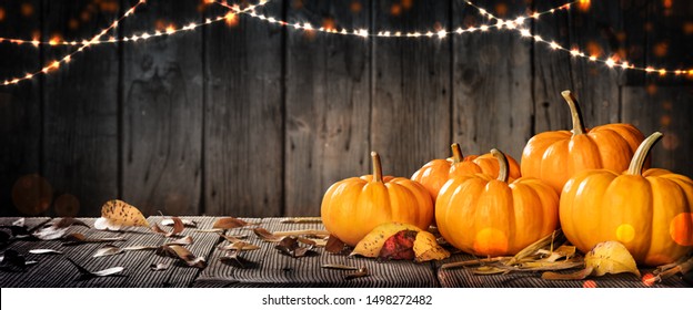 Thanksgiving Pumpkins And Leaves On Rustic Wooden Table With Lights And Bokeh On Wood Background - Thanksgiving / Harvest Concept