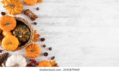 Thanksgiving still life with small orange, white, and green pumpkins, cinnamon sticks, pinecones, and dried leaves in a woven basket on a light wood surface - Powered by Shutterstock