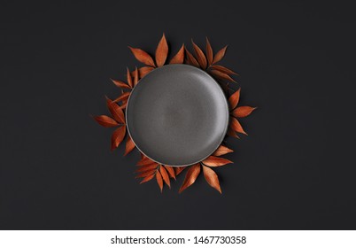 Thanksgiving Table With An Empty Grey Plate And Orange Leaves Decoration On A Black Background. Autumn Food Background. Above View Of An Empty Dish.