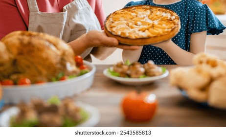 Thanksgiving table; roasted turkey in light-gray dish with tomatoes, woman in red apron, child in blue dress, rustic wood table, autumn foods, warm family atmosphere - Powered by Shutterstock