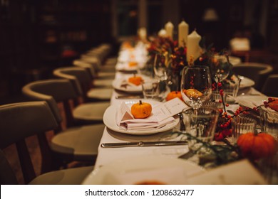 Thanksgiving table setting with autumn decorations, pumpkins, glasses and plates. Holidays, catering and hospitality concept.