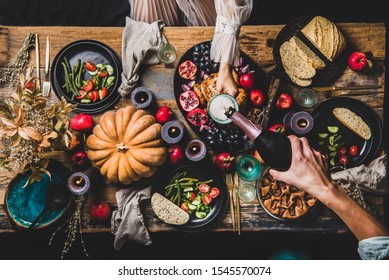 Thanksgiving table setting for family gathering. Flat-lay of man pouring champagne to glass at festive table with roasted chicken, vegetables, fig pie, fruit, candles over wooden background, top view - Shutterstock ID 1545570074