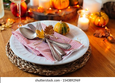 Thanksgiving Table Setting With Old Cutlery, Small Pumpkins, Candles And Orange Lights Garland In A Rustic Style