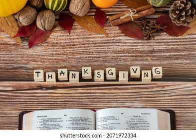 Thanksgiving Word On Wooden Cubes With Handwritten Letters, Open Holy Bible Book, And Fall Fruits On Wooden Table. A Christian Thanksgiving Concept. Top View. Giving Thanks To God Jesus Christ.