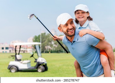That was a good game. Cheerful young man piggybacking his son while standing on golf course