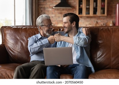 That is great. Excited diverse age males senior father young adult son sit on sofa bump fists embrace. Grown grandson old grandfather celebrate soccer team victory after watching sport game on laptop