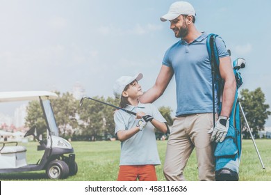 That was a great game! Smiling young man and his son looking at each other while standing on the golf course