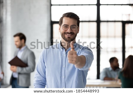 That is great! Satisfied loyal young male client of bank agency company posing for portrait in office looking at camera with happy smile raising thumb up showing positive feedback to service received