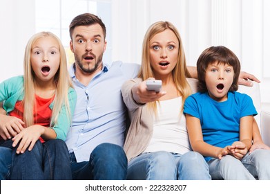 That is just amazing! Surprised family of four bonding to each other and keeping mouth open while watching TV at home together  - Powered by Shutterstock