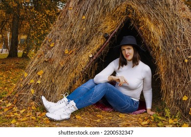 Thatched Hut In The Autumn Forest. Cabin In The Countryside. Happy Woman Is Resting In Nature. Escape From The Bustle Of The City To Nature.