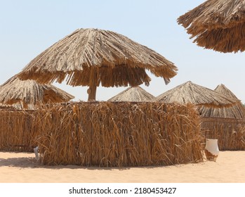 Thatched Sunshades And Sunbeds For Tourists, On A Yellow Sand Beach. Sun Umbrellas Near The Egyptian Hotel. Concept Of Sea Vacations And Relaxation. Empty Sun Loungers, Minimal Photo In Beige Tones.