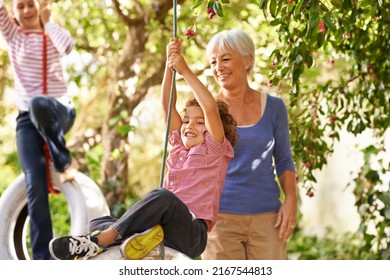 Thats how you do it. Shot of a woman helping her grandson on a tire swing with her granddaughter in the background. - Powered by Shutterstock