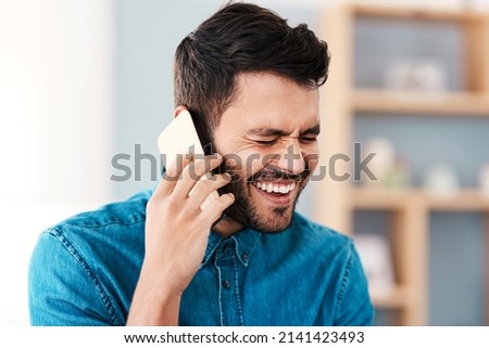 Thats incredibly hilarious. Cropped shot of a handsome young man laughing while taking a phonecall in his living room at home.
