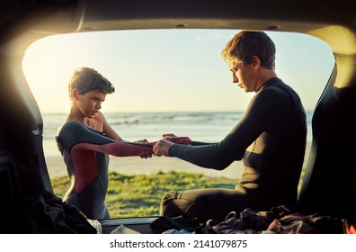 Thats what big brothers are for. Shot of a young surfer helping his little brother put on his wetsuit at the beach. - Powered by Shutterstock