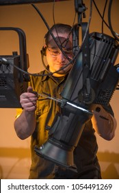 Theater Lighting Technician Adjusting Focus Of Lighting Elements Backstage Next To A Let Cyclorama Curtain.