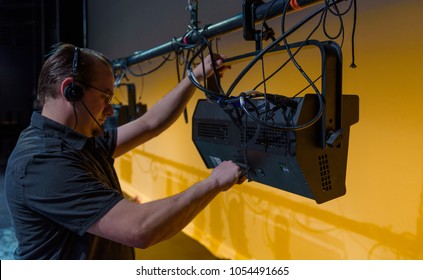 Theater Lighting Technician Adjusting Focus Of Lighting Elements Backstage Next To A Let Cyclorama Curtain.