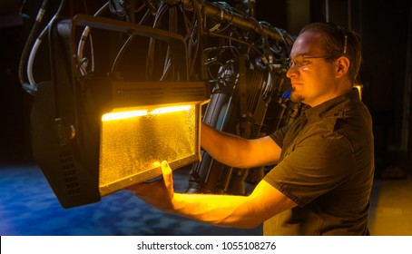 Theater Lighting Technician Adjusting Focus Of Lighting Elements Backstage Next To A Let Cyclorama Curtain.