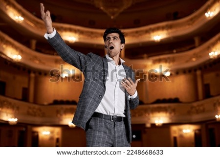 Theatre play a young actor in original image. Sincere emotions transmitted camera. Photo for cultural and fashion magazines, posters and websites. Brunette male in gray suit singing, gesturing