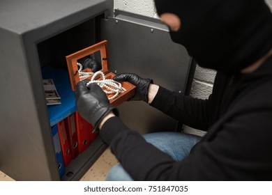 theft, burglary and people concept - thief in mask stealing valuables from safe at crime scene