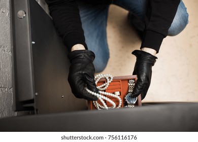 theft, burglary and people concept - thief stealing valuables from safe at crime scene
