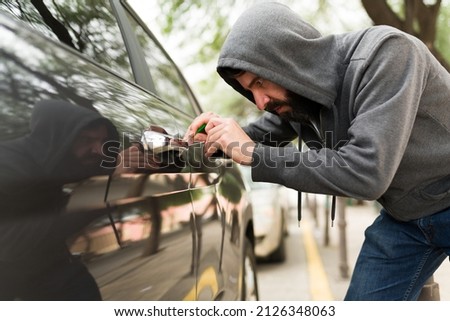 Theft criminal committing carjacking and using a screwdriver to open a car to steal it on the street