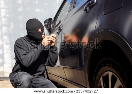 Theft with mask trying to break into the car using screwdriver. Street criminal and car thief, car theft concept