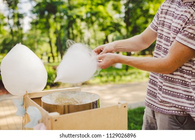 Theme is a family small business cooking sweets. Hands close-up A young male shopkeeper holding a merchant makes candy floss, fairy floss or Cotton candy in summer park.