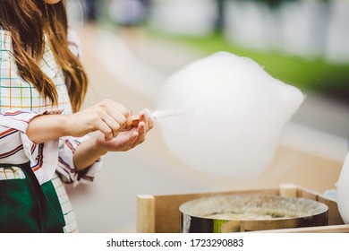 Theme is a family small business cooking sweets. Hands close-up Young woman trader owner of the outlet makes a candy floss, fairy floss or Cotton candy in the park in summer.