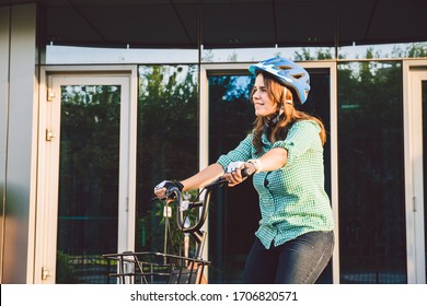 Theme to work on the bike. A young Caucasian woman arrived on environmentally friendly transport bike to the office. Girl in a bicycle parking office building in a helmet, gloves and shirt and jeans.
