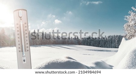 Themometer with minus temperatures in Celsius in front of a winter landscape